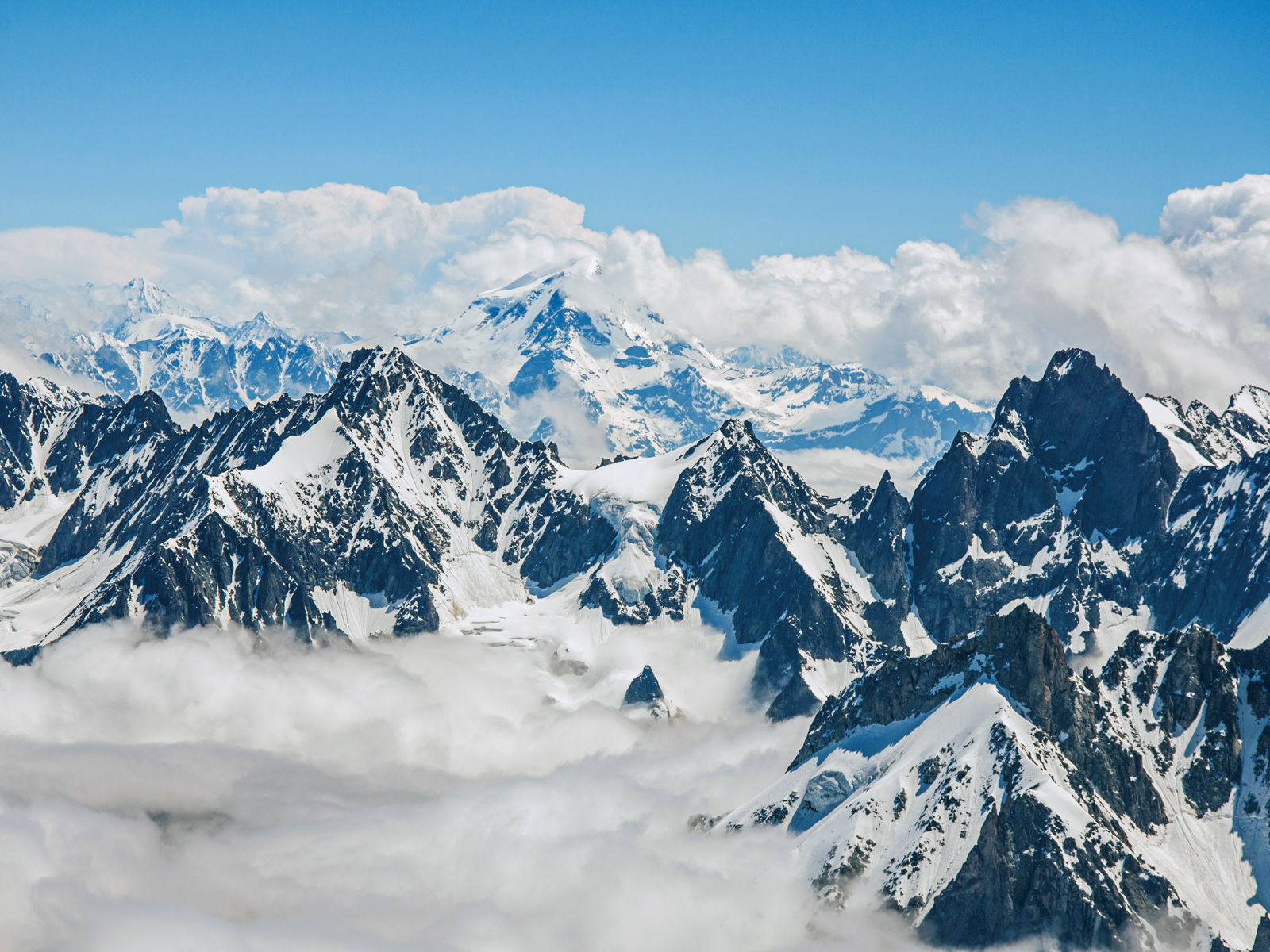 Alpeilla korkeita lumihuippuisia vuoria, taustalla sininen taivas