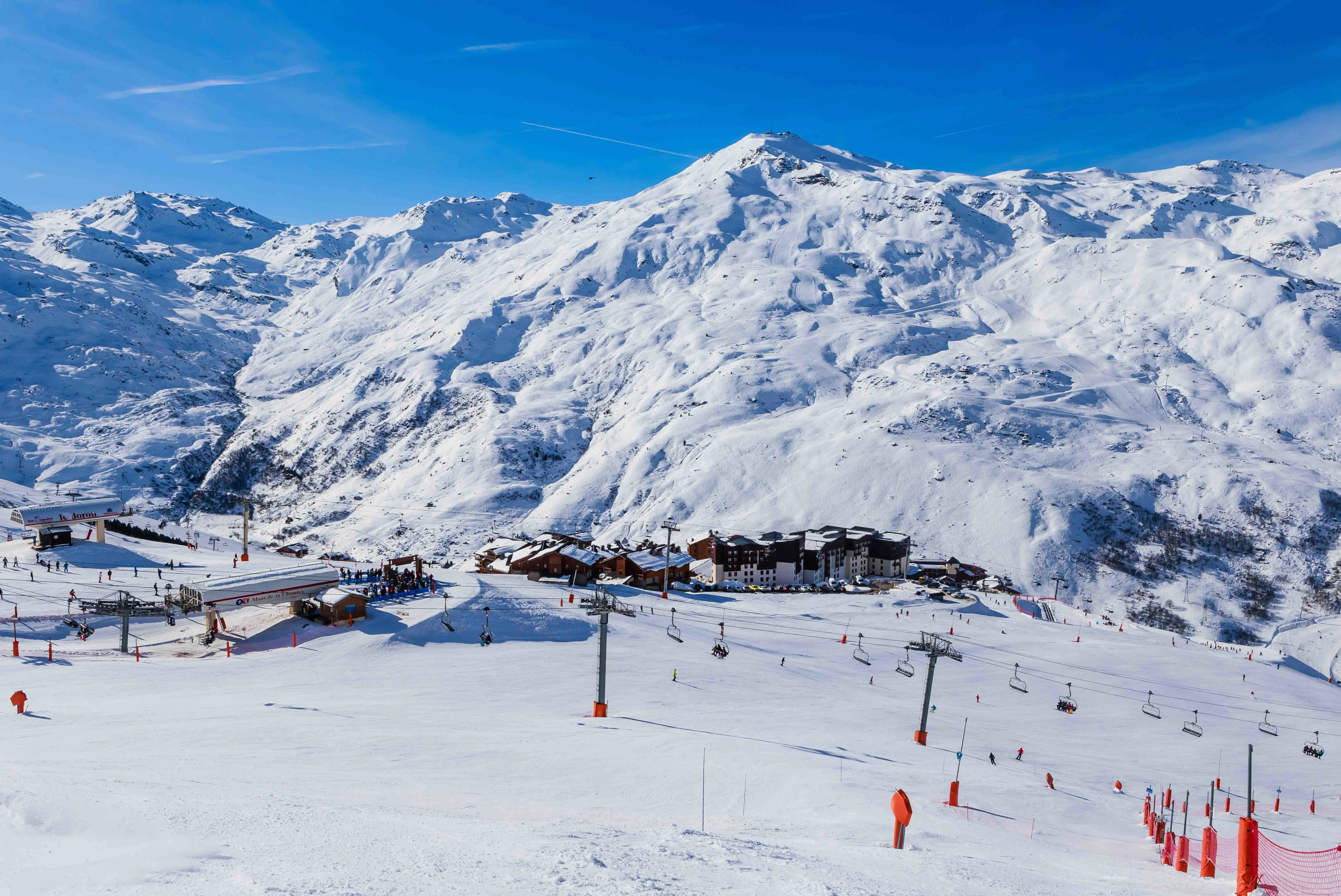 Travel to Val Thorens - Winter wonderland with ski slopes and lifts in a snow-capped mountain resort, skiers enjoy sunny weather.