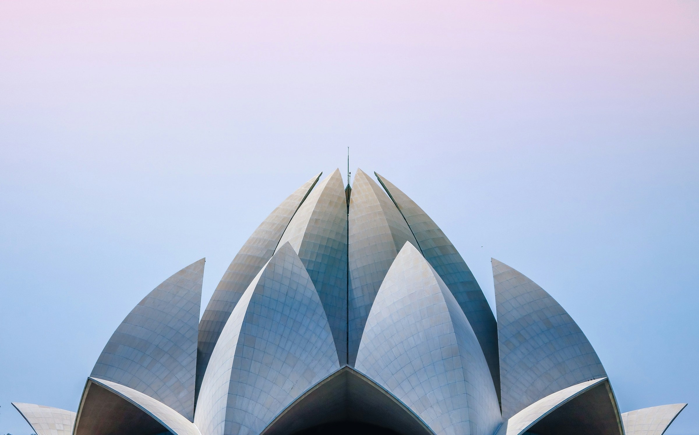 Symmetrinen näkymä modernista rakennuksesta, jossa on lootusmainen rakenne pastellinväristä taivasta vasten Delhissä.