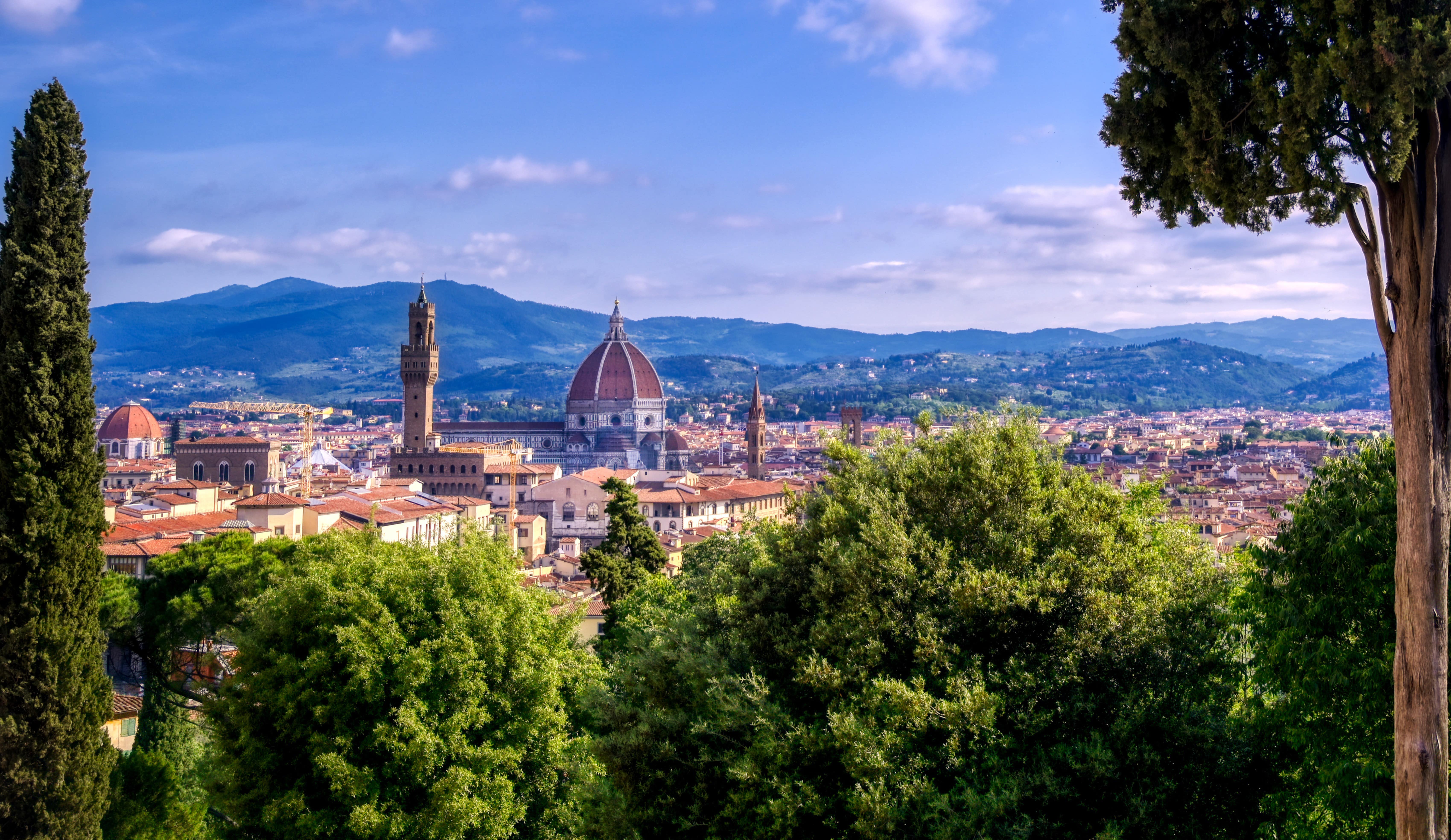 Matkusta Firenzeen - Näkymä korkealta Firenzen yltä Italiassa, jossa vehreät puut kohtaavat kaupungin kuuluisalla kirkolla ja sinisellä taivaalla taustalla