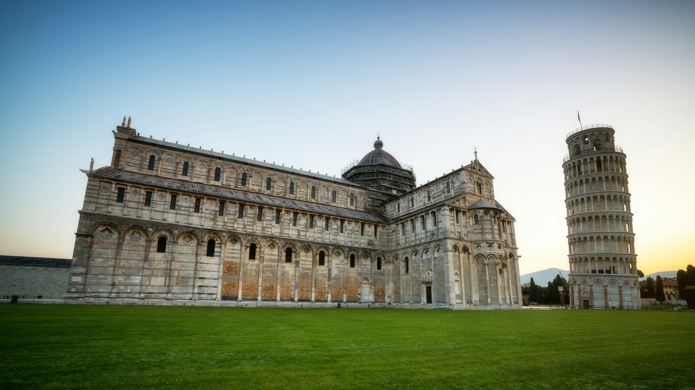 Vacker traditionell Italiensk vit byggnad på en gräsmatta med lutande tornet i Pisa bredvid