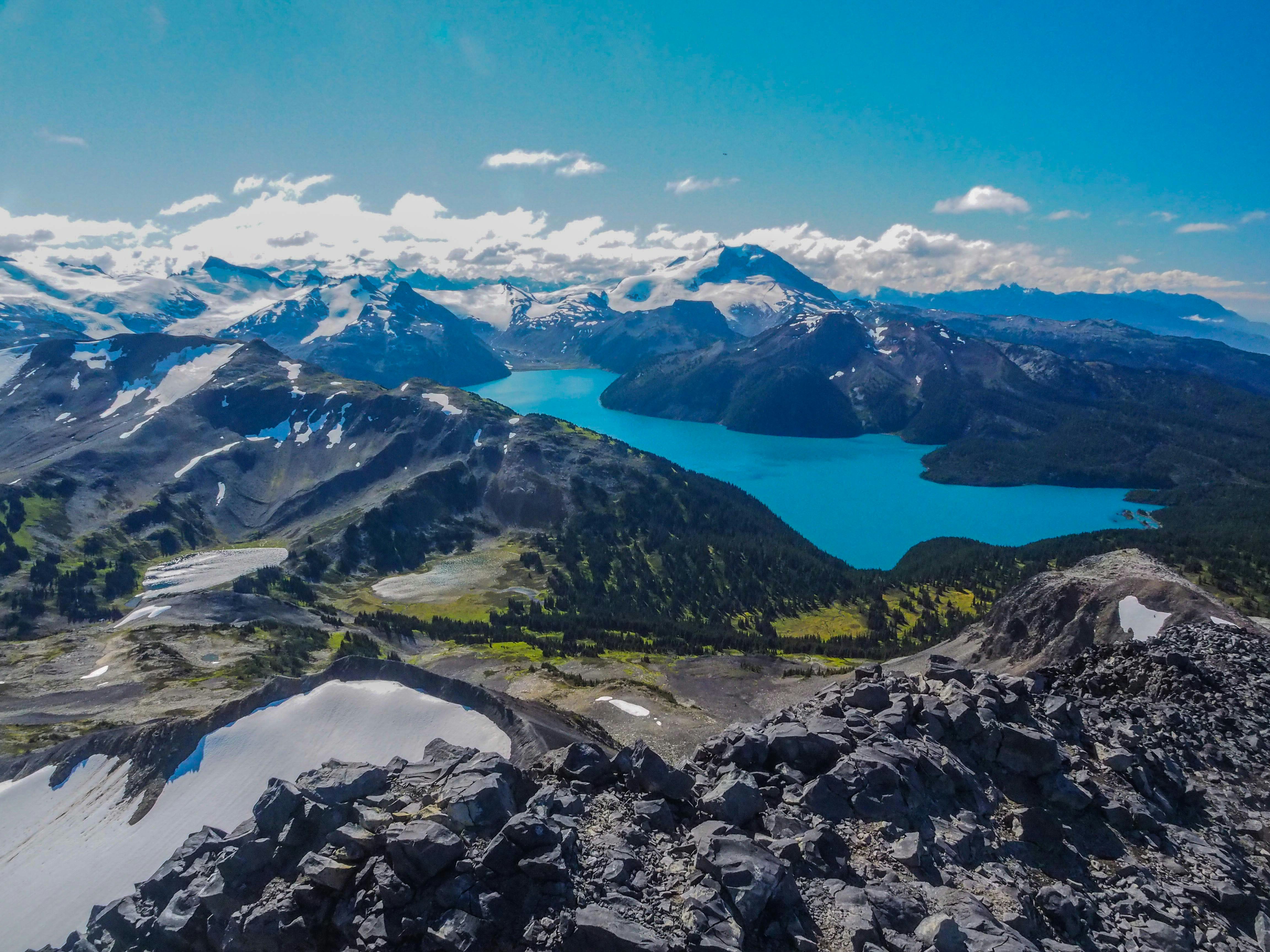 Matkusta Whistleriin - Panoraamanäkymä turkoosille vuoristojärvelle, jota ympäröivät lumihuippuiset huiput ja kivinen maasto vuoristoisessa maisemassa