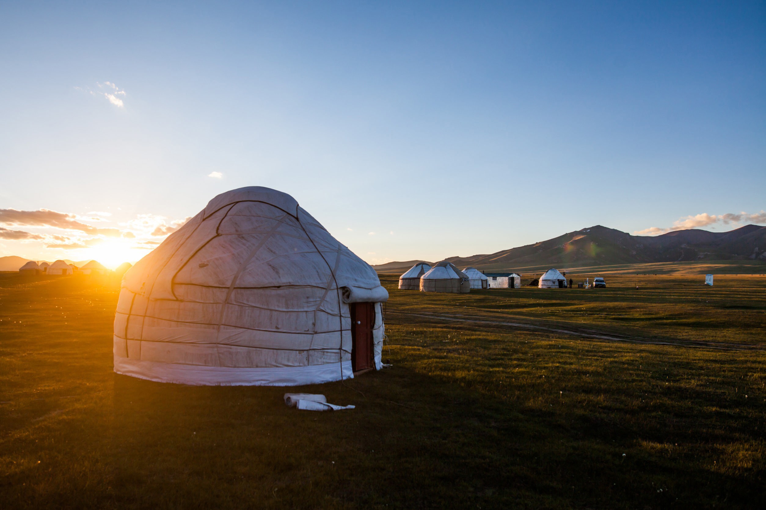 Klassisk mongolisk hydda på en slätt med vacker solnedgång i bakgrunden bland bergen