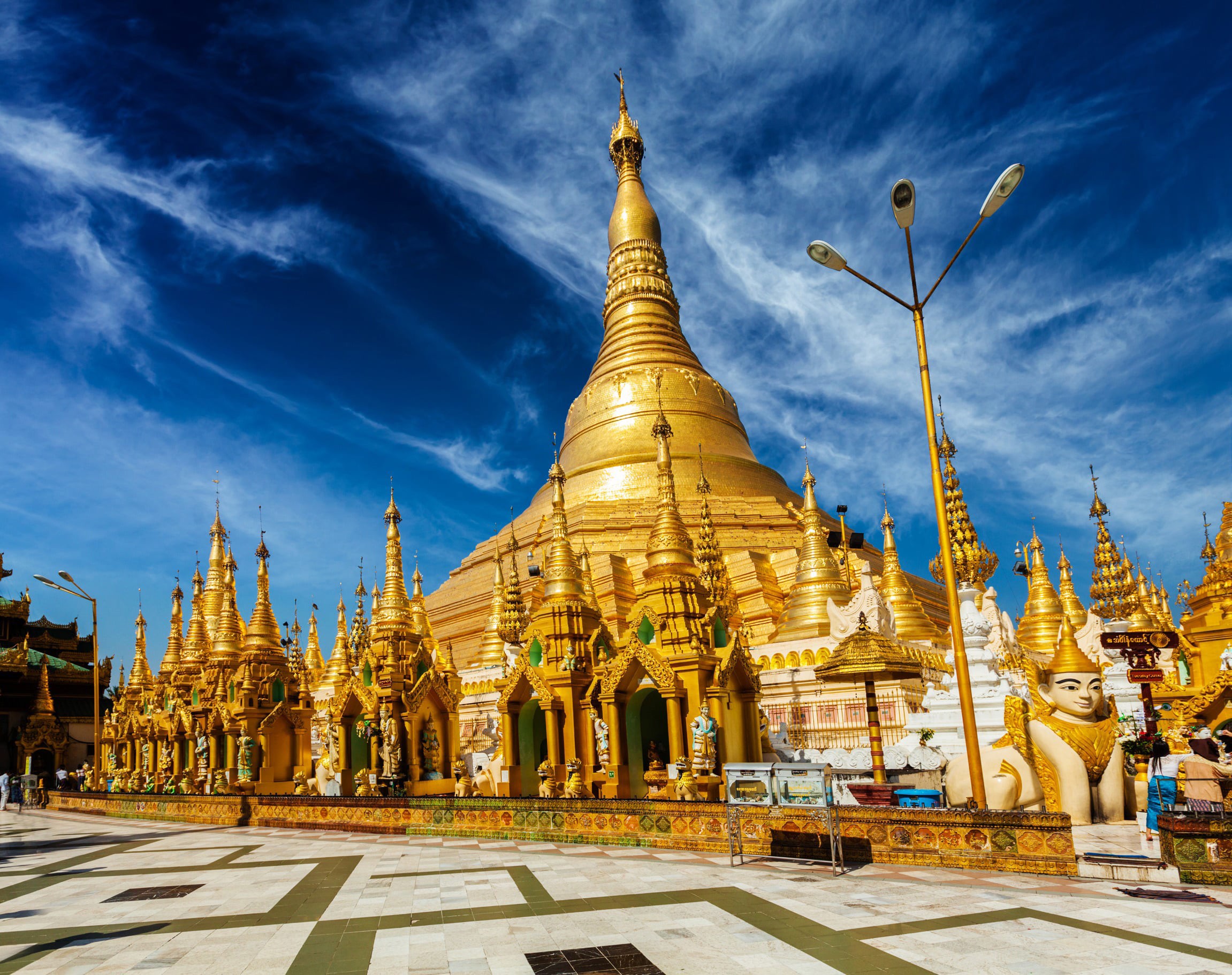 Vy snett nedanifrån på känt tempel i guld och juveler i Myanmar med vacker blå himmel i bakgrunden