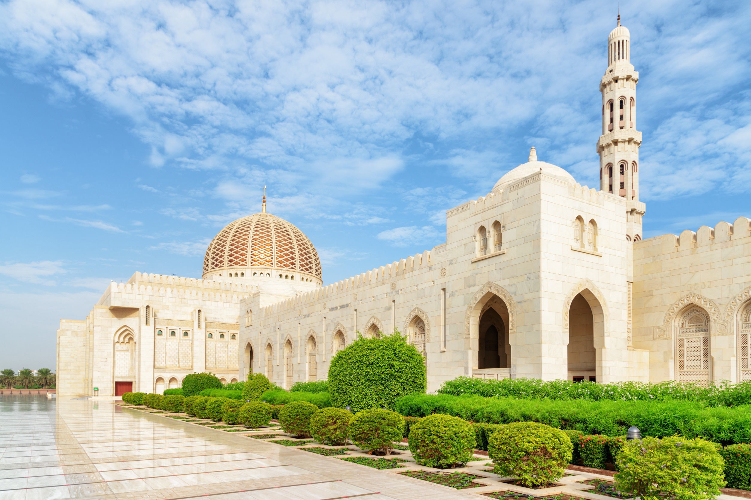 Vacker vit moské i Muscat med gröna buskar omkring sig och klarblå himmel i bakgrunden