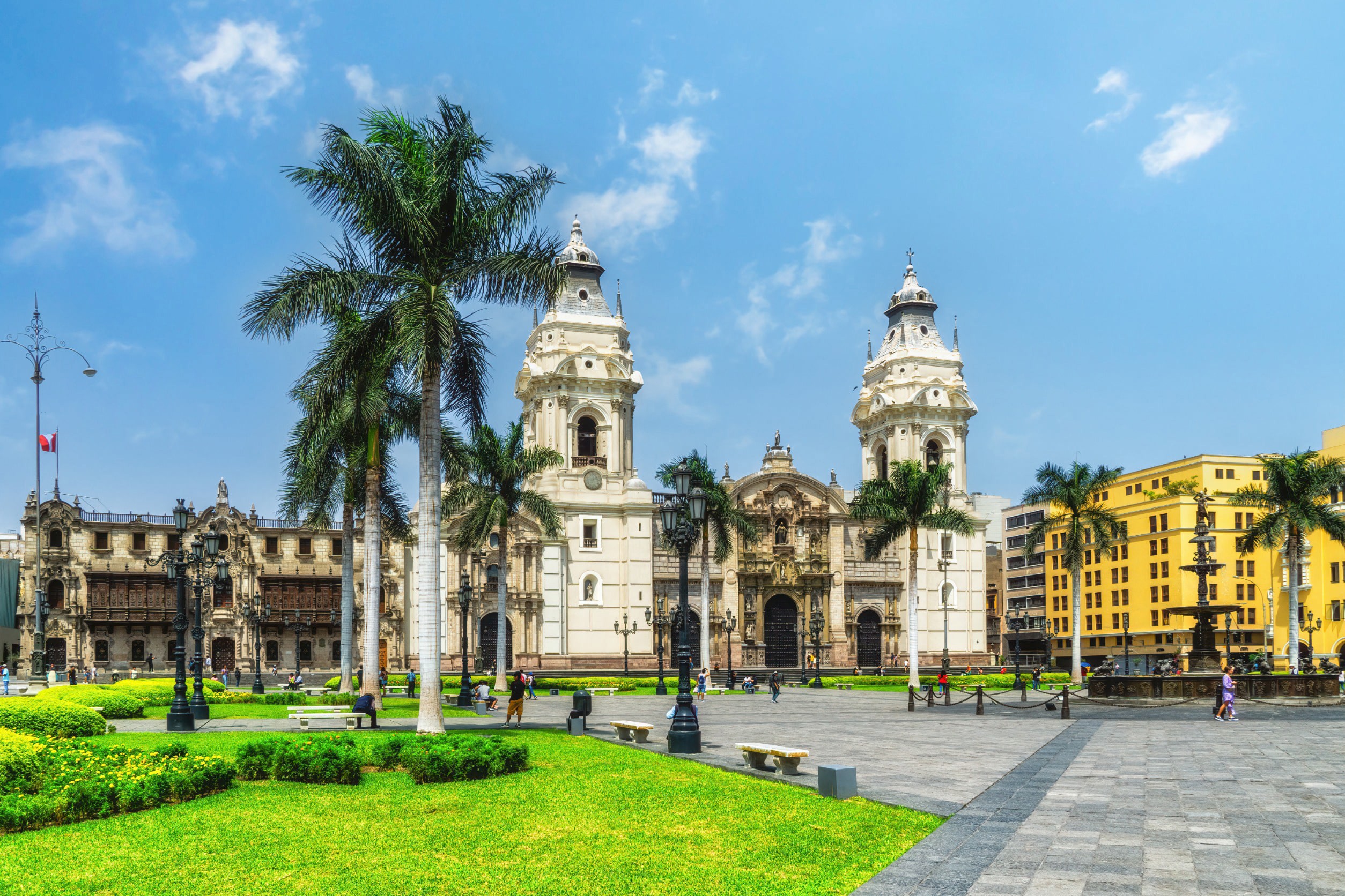 Vackert torg men grönt gräs, palmer och traditionella spanska byggnader i vit och gult i Lima, Peru