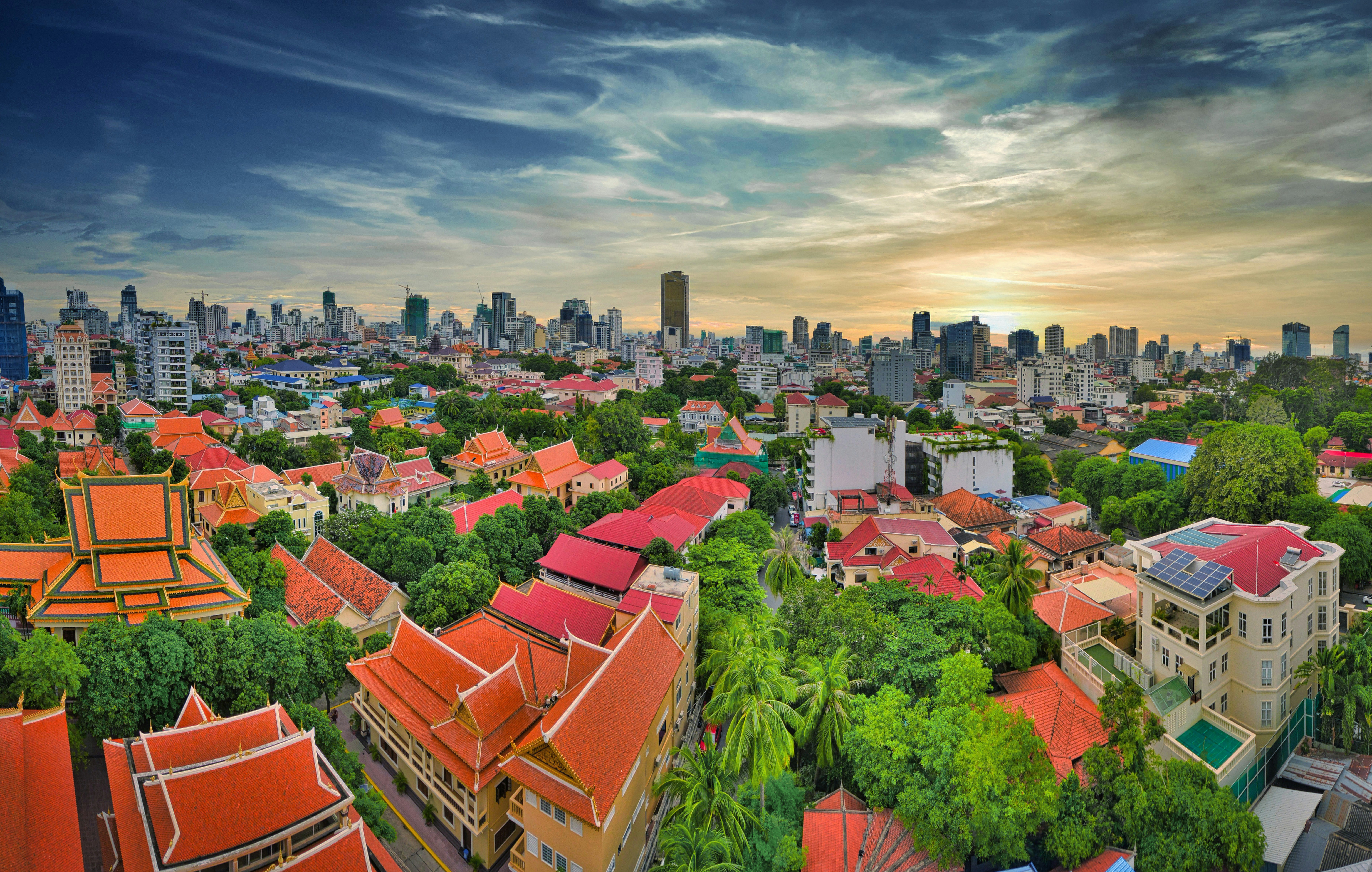 Resa till Phnom Penh - Panoramautsikt över Phnom Penh vid solnedgången med traditionella och moderna byggnader omgivna av grönskande träd.