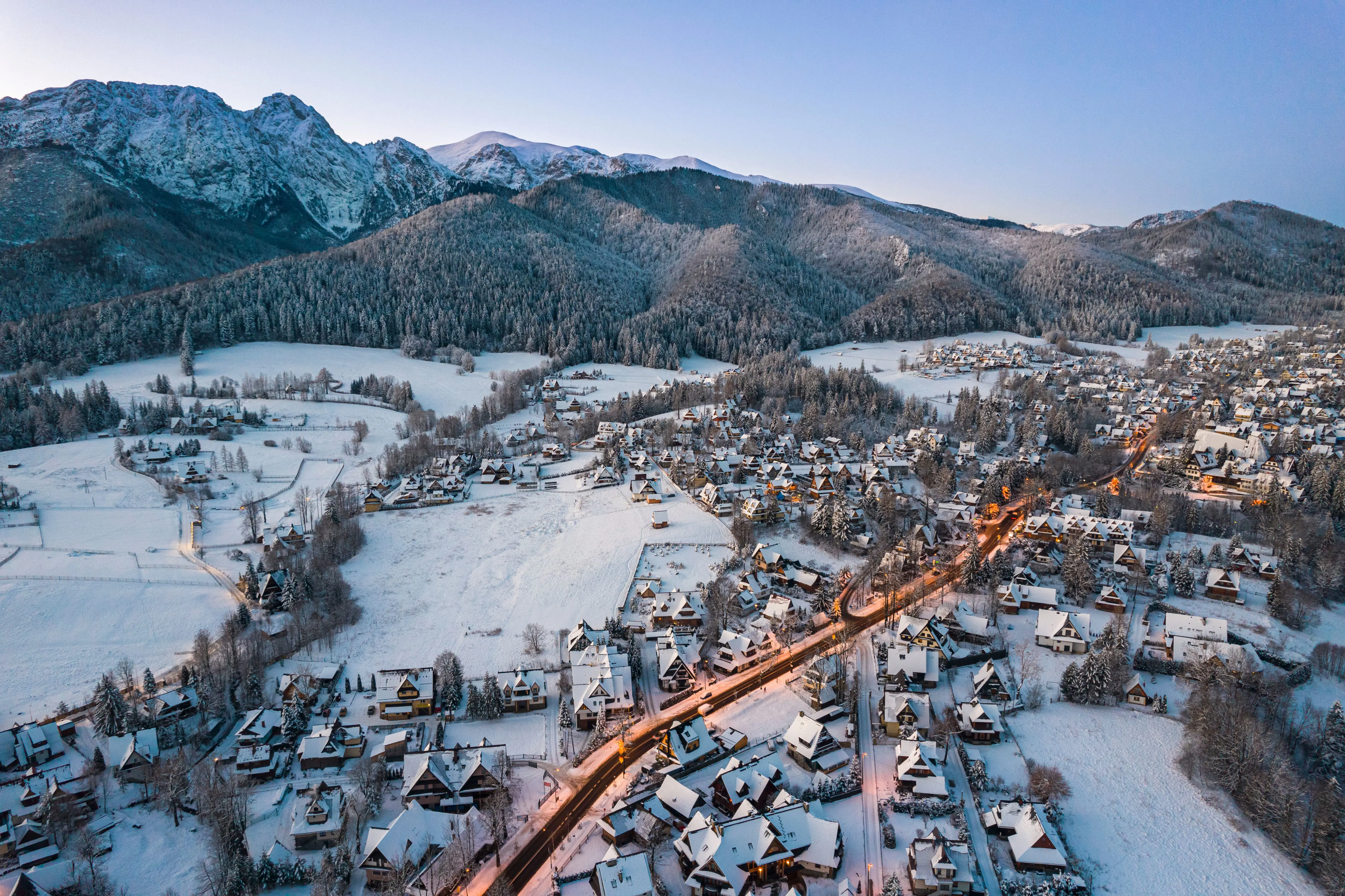 Resa till Zakopane - Panoramisk vy över snötäckt stad i en dal under en solnedgång med berg i bakgrunden