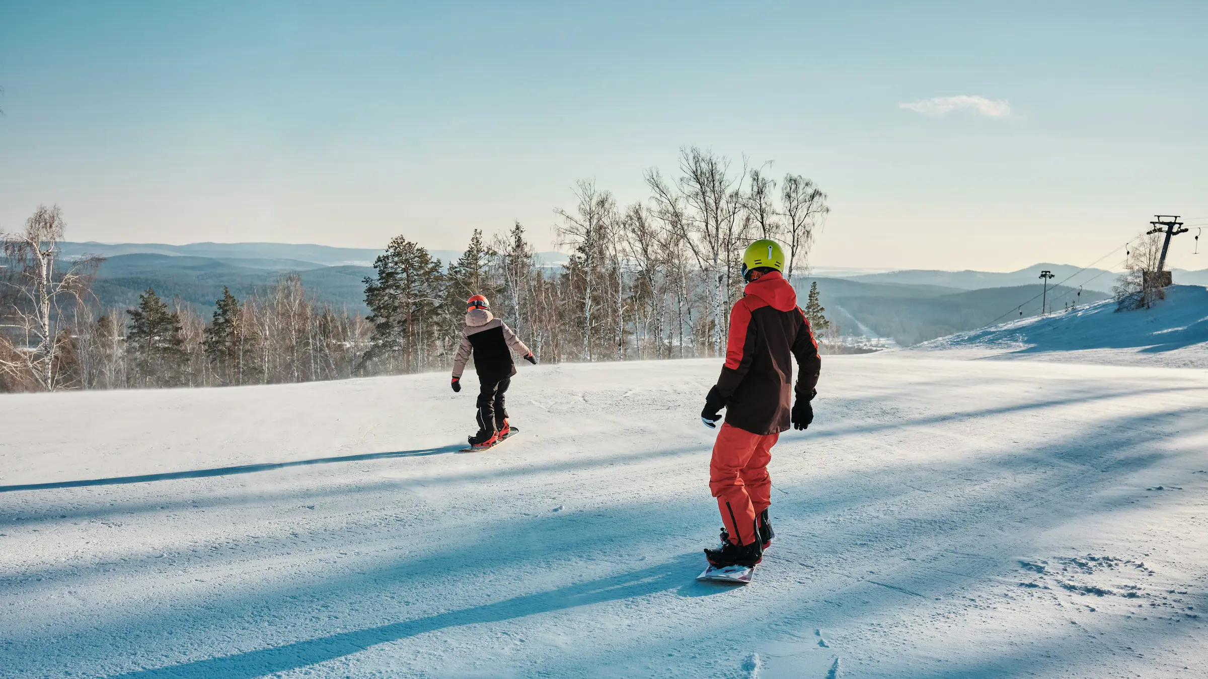 Travel to Sälen - Two people snowboard down a snow-covered slope with views of trees and mountains