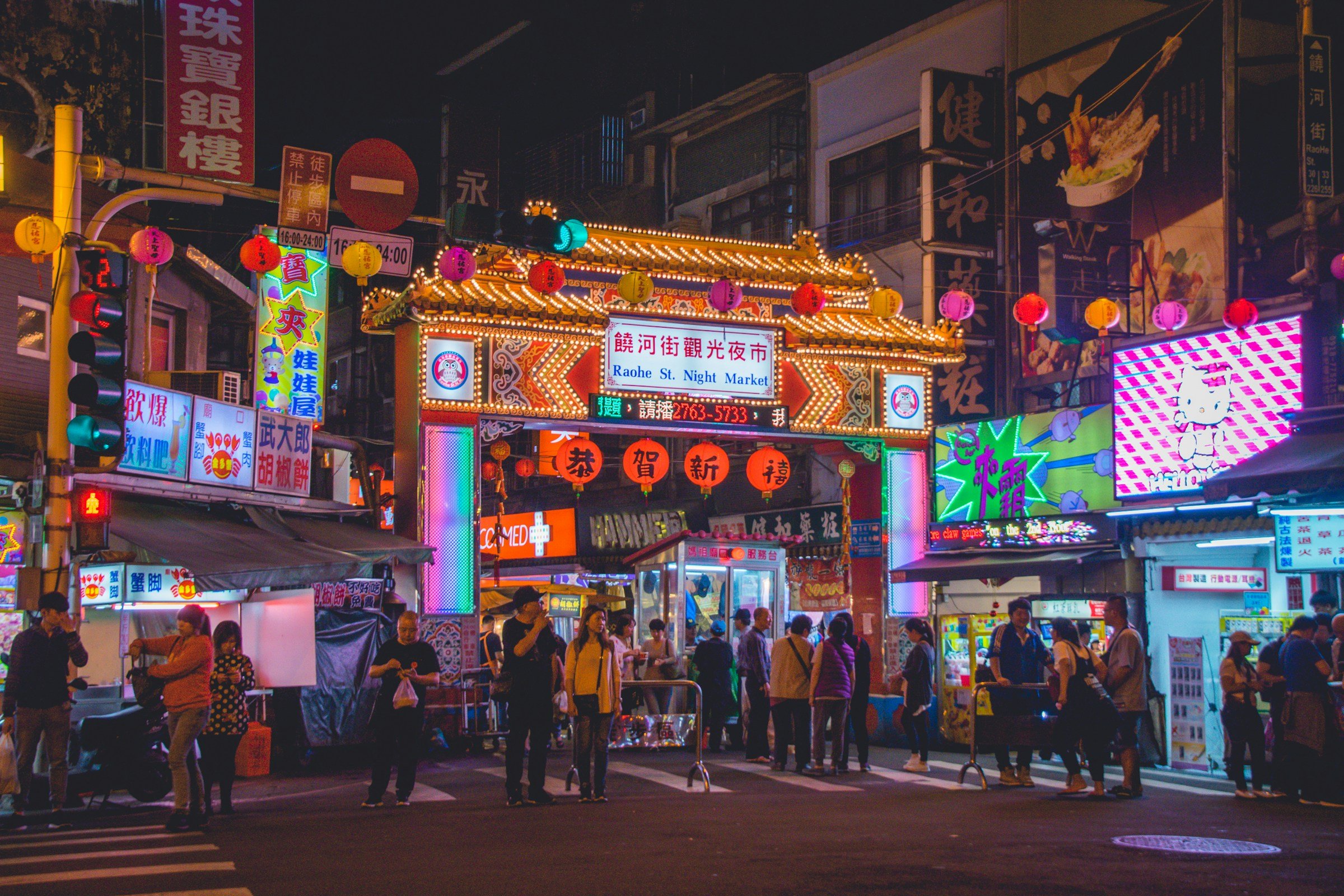 Ingång till känd nattmarknad i Taipei-stad med neon ljus, skyltar och folk omkring