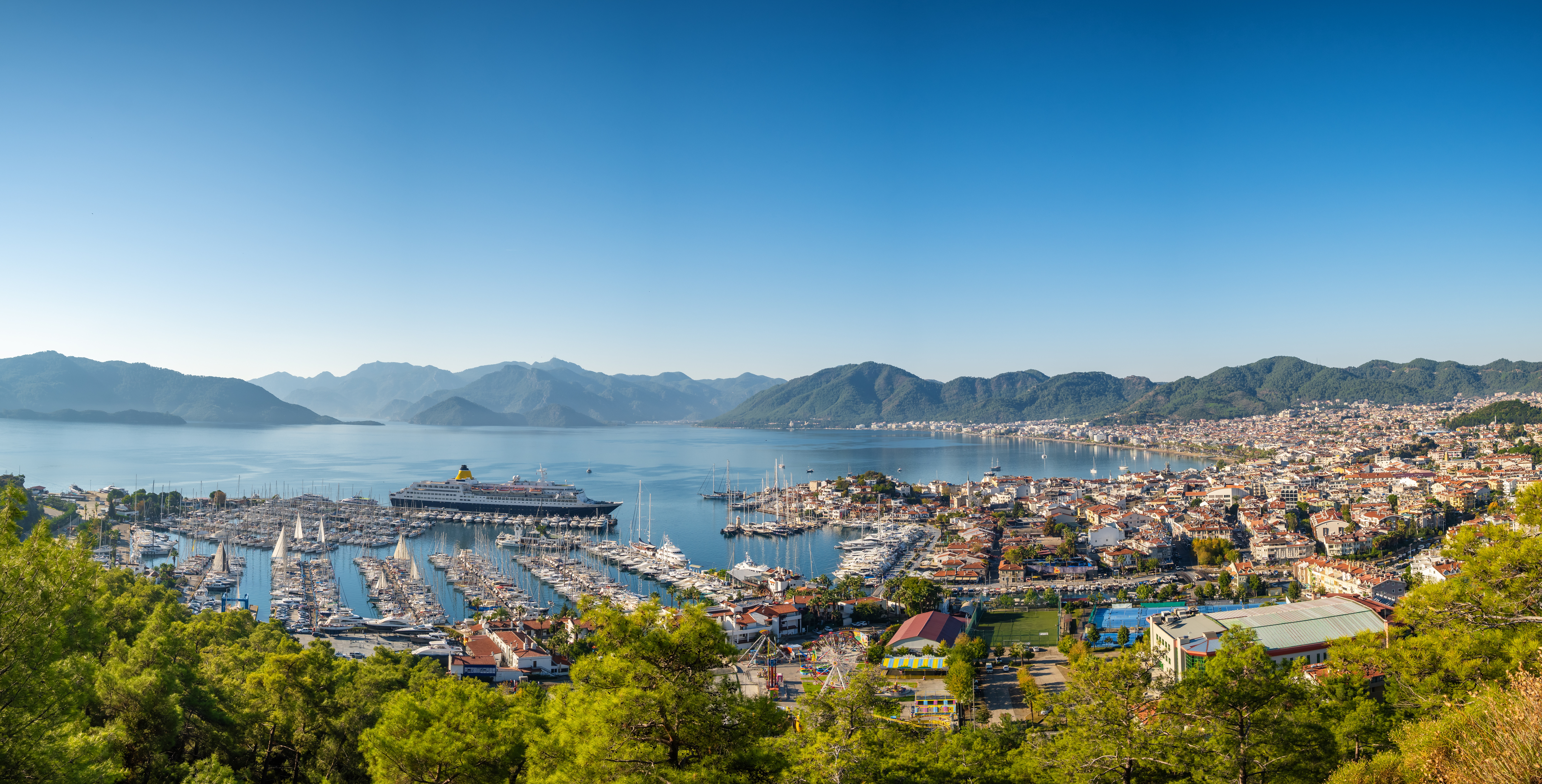 Resa till Marmaris - Panorama vy över Marmaris-stad med grönskande träd, byggnader, havet och stränder som möts av en blå himmel