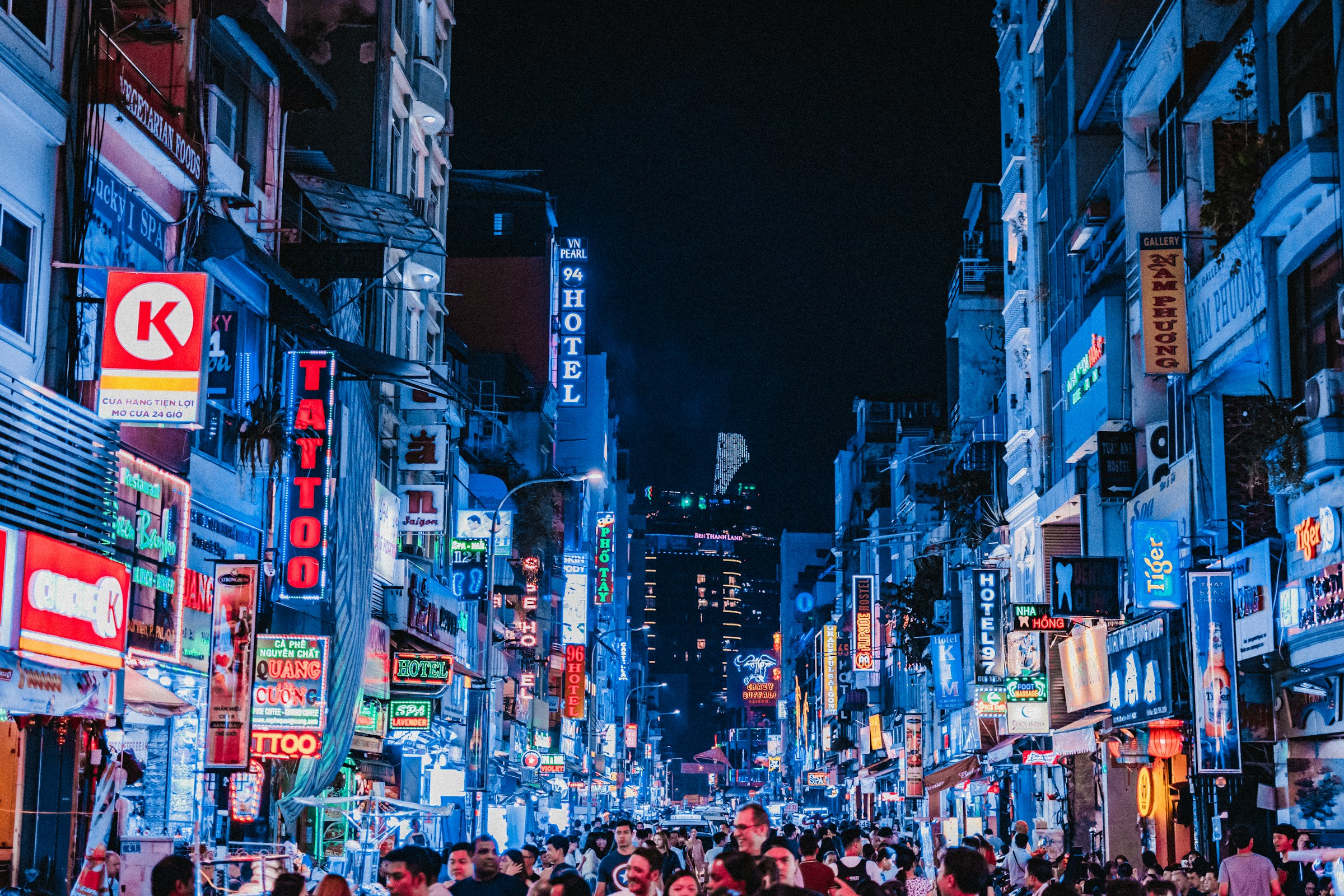 Livlig stadsgata på kvällen i Ho Chi Minh City med neonljus och skyltar, folksamling promenerar i storstadsatmosfär.